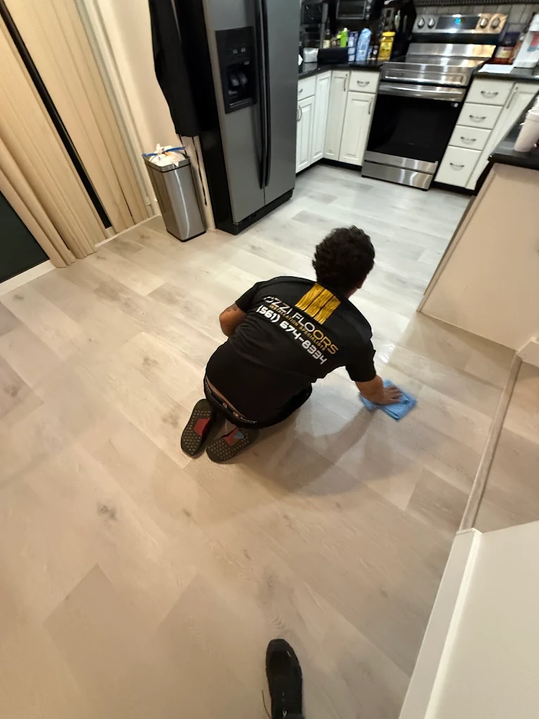An Ozzifloors installer kneeling in a kitchen, wiping down a newly installed light plank floor
