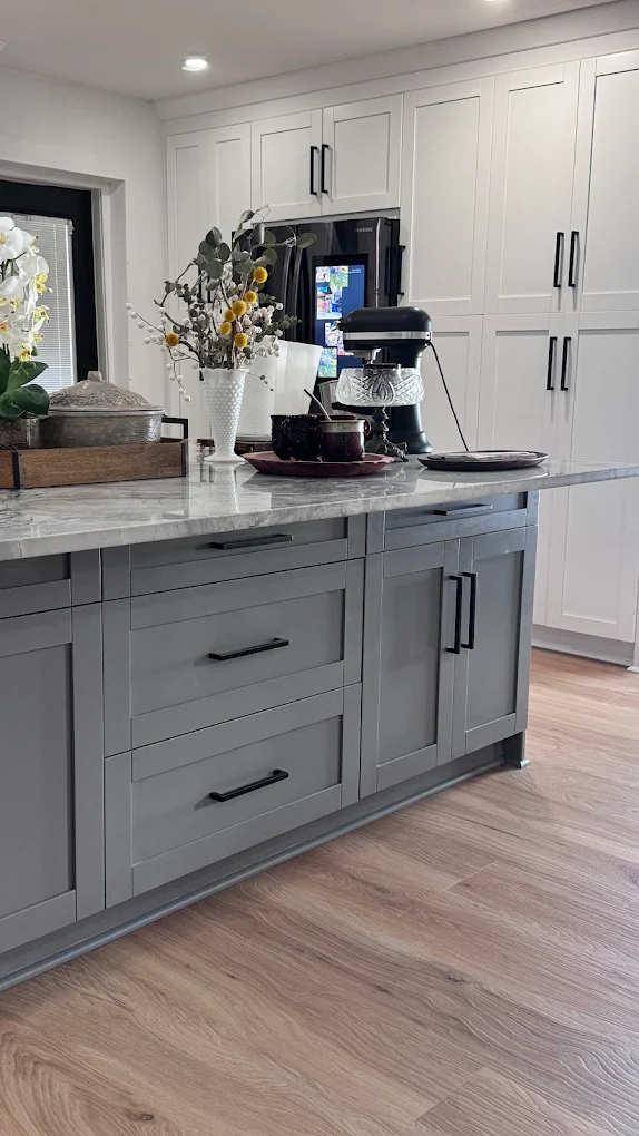 Light plank flooring installed by Ozzifloors running under a grey kitchen island with white cabinets behind it